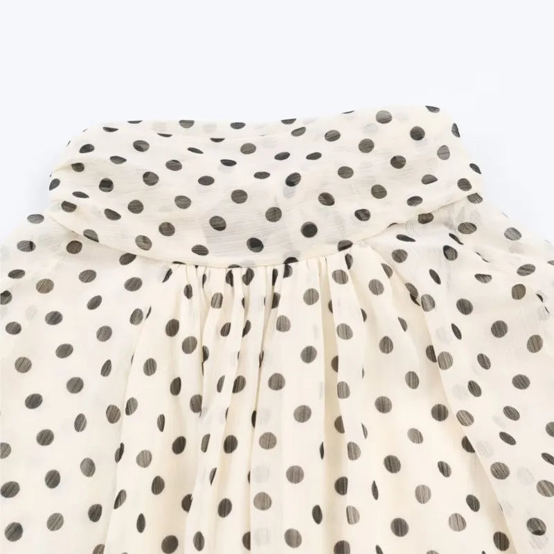 Polka dot tie-neck blouse close-up with gathered yoke and soft ruffled collar.